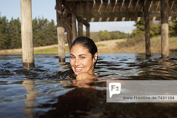Porträt einer lächelnden Frau  die im See unter dem Dock schwimmt.