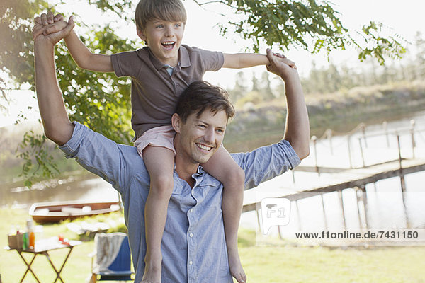 Vater trägt lächelnden Sohn auf den Schultern am Seeufer