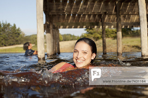 Porträt einer lächelnden Frau  die im See unter dem Dock schwimmt.