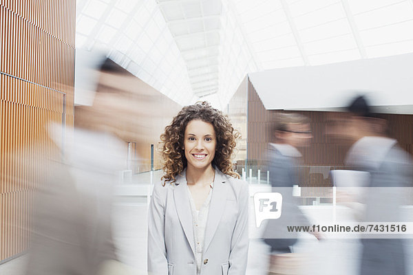 Portrait of smiling woman with co-workers rushing by in lobby