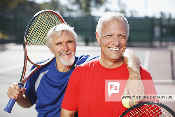 Ältere Männer lächeln auf dem Tennisplatz
