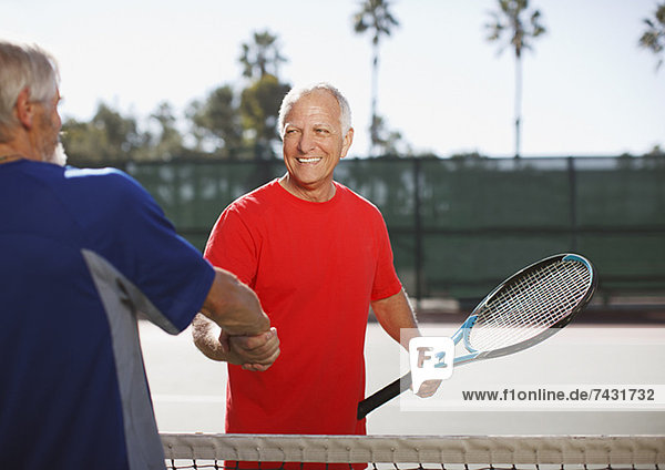 Ältere Männer beim Händeschütteln auf dem Tennisplatz