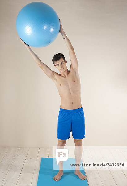 junger Mann macht Gymnastikübungen mit einem Gymnastikball auf einer Gymnastikmatte