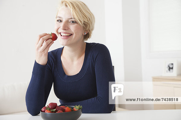 Caucasian woman eating strawberries in kitchen