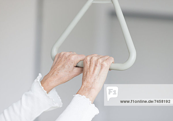 Hände einer Seniorin am Haltegriff eines Krankenbettes