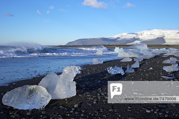 Icebergs on volcanic sand beach at Jokulsarlon with snow on the massive icecap of Vatnajokull behind  Iceland  Polar Regions