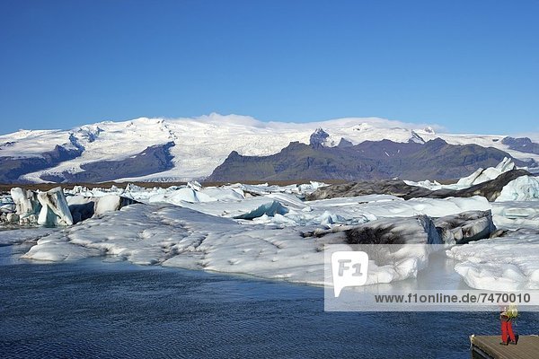 Man taking photo of icebergs on the glacial lake at Jokulsarlon with snow on the massive icecap of Vatnajokull behind  Iceland  Polar Regions