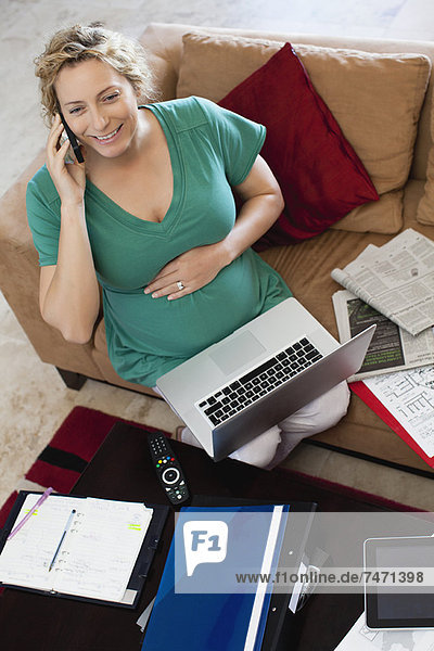 Schwangere Frau am Telefon und Laptop