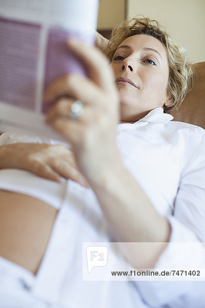 Schwangere lesend auf dem Sofa