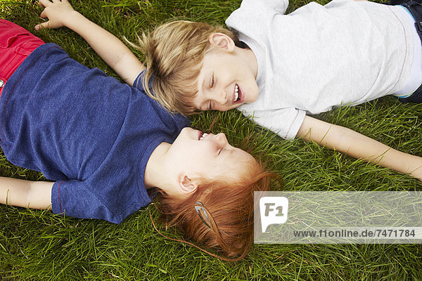 Lächelnde Kinder  die zusammen im Gras liegen.