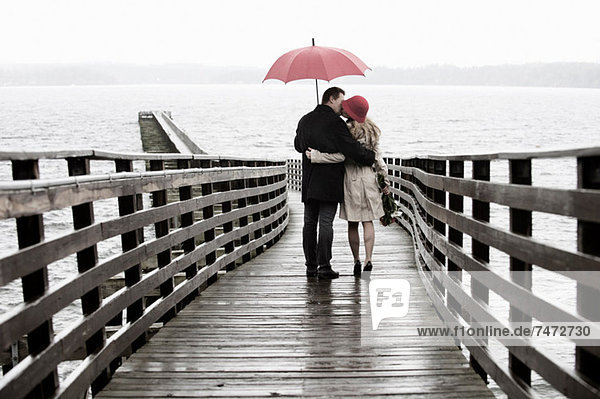 Couple kissing on wooden pier in rain