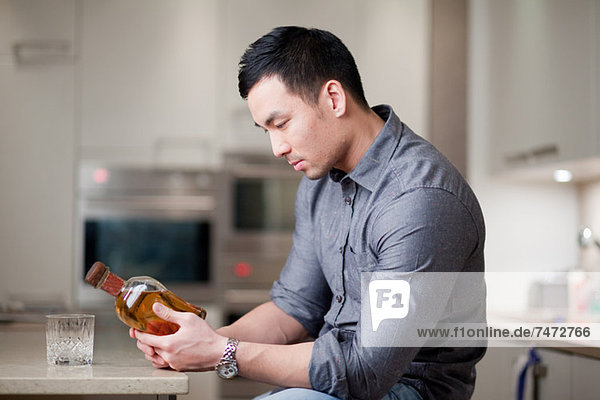 Mann untersucht Whiskeyflasche in der Küche