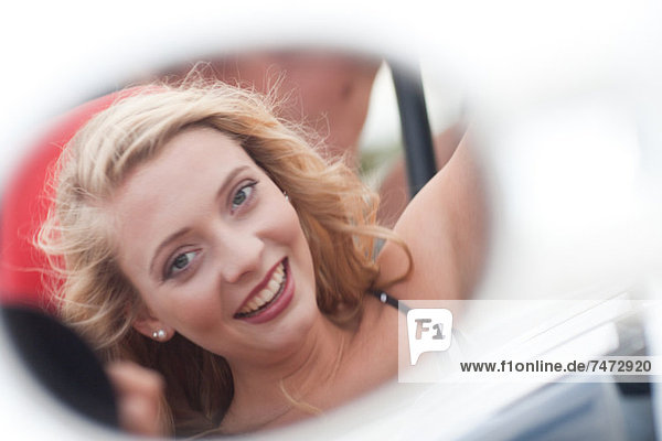 Lächelnde Frau reflektiert im Autospiegel