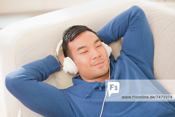 Mann hört Kopfhörer auf dem Sofa