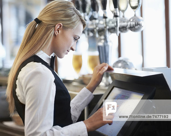 Young waitress using computer at restaurant counter