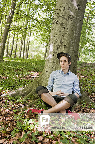 Young man sitting in front of a tree in the woods  Sweden  Europe