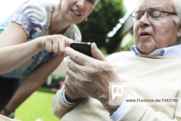 Young woman explaining to a senior citizen how to use a smartphone