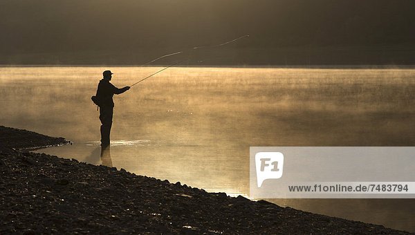 A fly fisherman standing on the shore of the Obernau reservoir at sunrise  Netphen  North Rhine-Westphalia  Germany  Europe