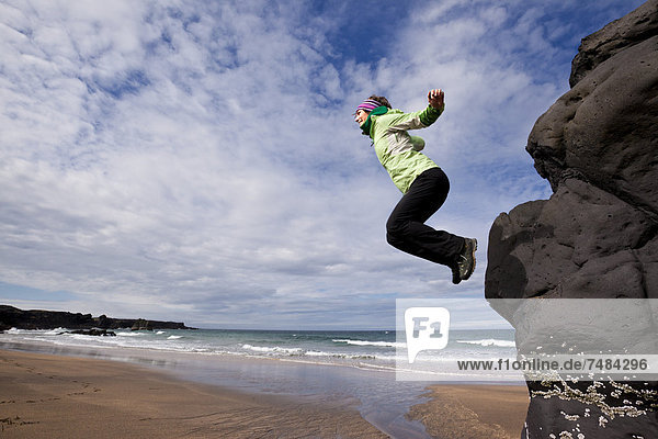 Young woman jumping a cliff on the coast  Iceland  Europe