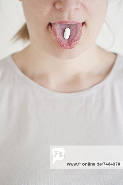 Woman with a white pill on her tongue