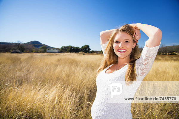 USA  Texas  Schwangere junge Frau im Gras stehend  lächelnd  Portrait