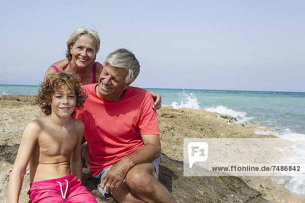Spanien  Großeltern mit Enkel am Strand sitzend  lächelnd