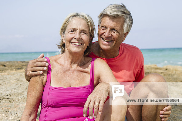 Spain  Senior couple sitting on rock at beach  smiling