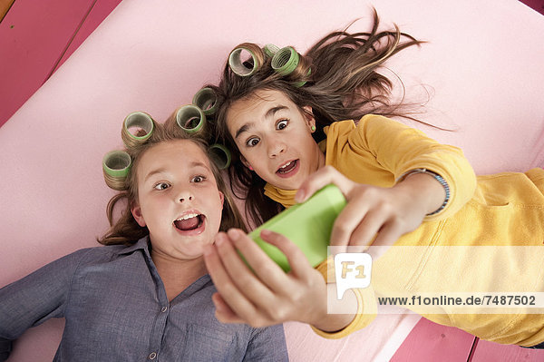 Mädchen mit Haarroller fotografieren sich selbst mit Smartphone