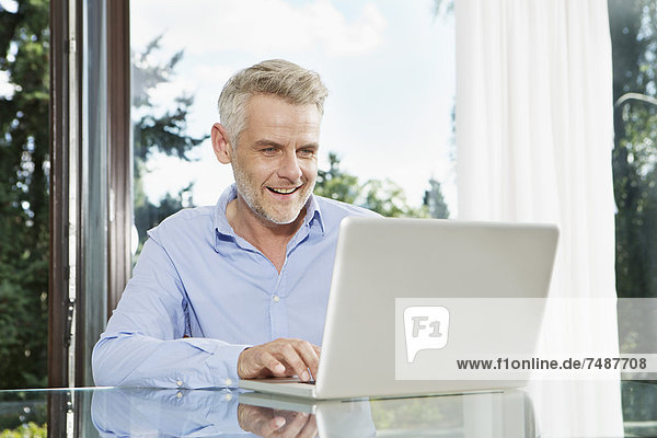 Mature man sitting at table and using laptop