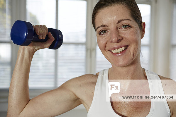 Mature woman exercising with barbell at home