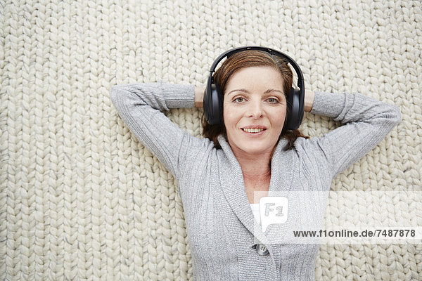 Reife Frau auf dem Teppich liegend und Musik hörend