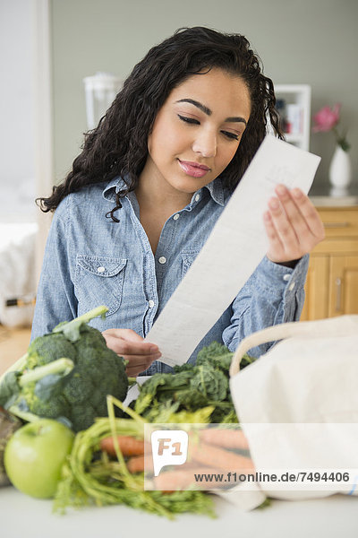 Hispanic woman reading grocery receipt