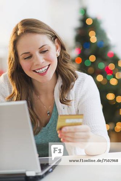 Young woman on-line shopping from home with Christmas tree on background