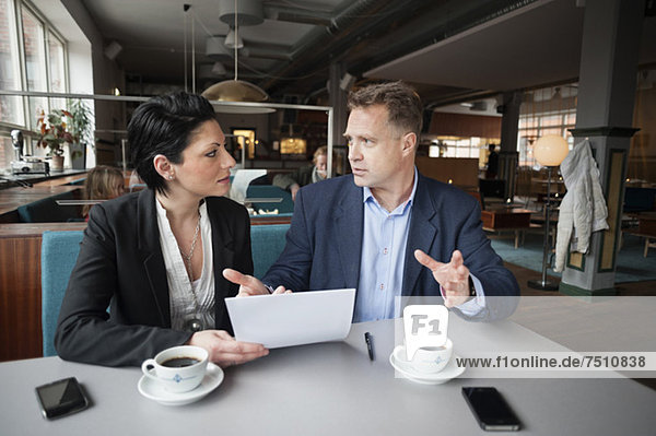 Reife Unternehmerin und Kollegin mit Papierkram am Kaffeetisch