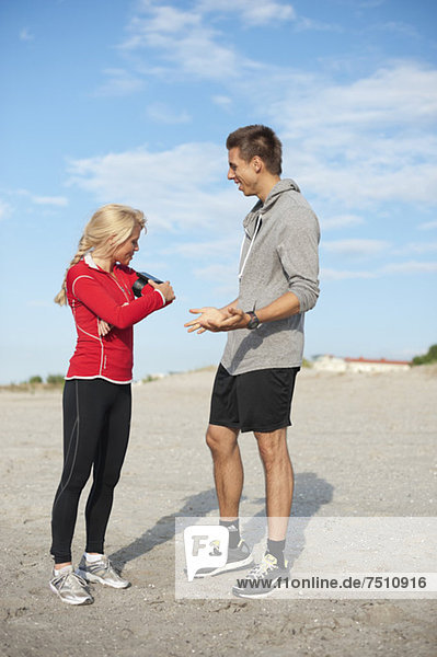 Volle Länge des jungen männlichen Joggers mit weiblichem Freund der den MP3-Player am Strand anpasst.
