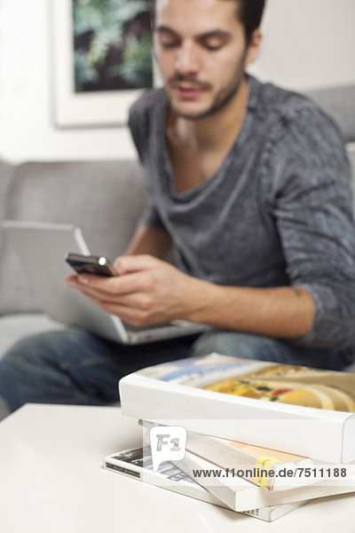 Junger Mann mit Handy und Laptop mit Bücherstapel im Vordergrund