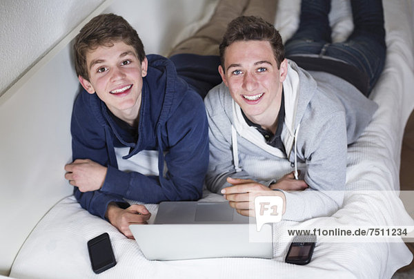 Portrait von glücklichen Jungen mit Laptop zu Hause im Bett liegend
