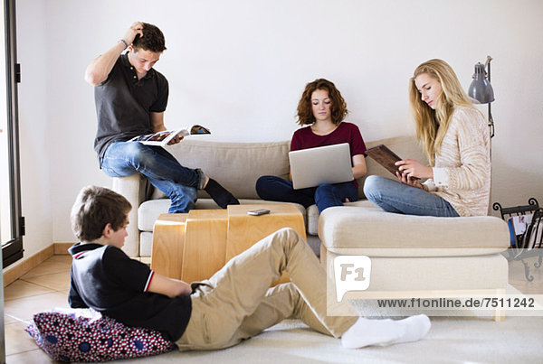 Junge Freunde mit Magazin  Laptop und digitalem Tablett im Wohnzimmer