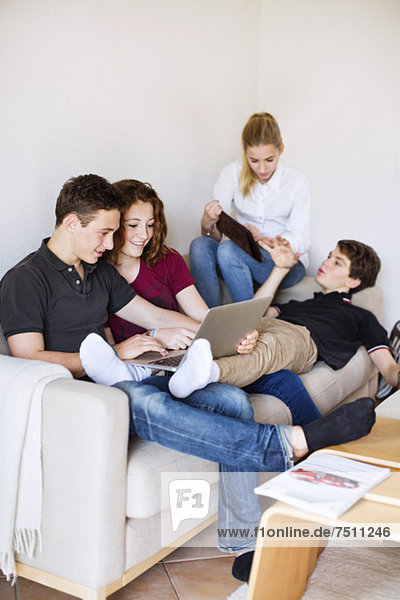 Junge Freunde mit Laptop und digitalem Tisch diskutieren im Wohnzimmer