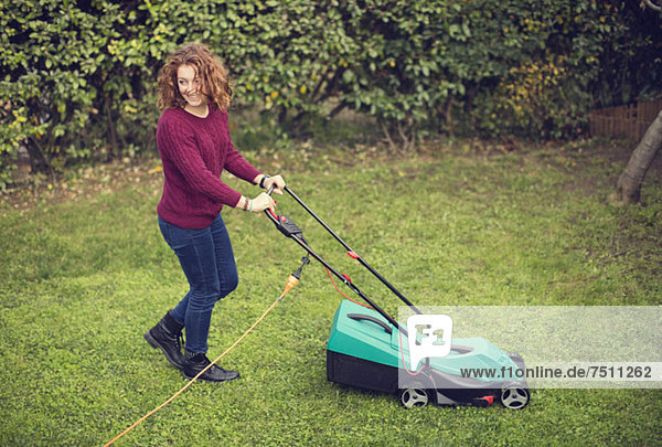 Fröhliches junges Mädchen schiebt elektrischen Rasenmäher auf Gras