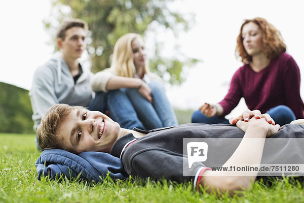 Porträt eines Jungen auf Gras liegend mit Freunden im Hintergrund