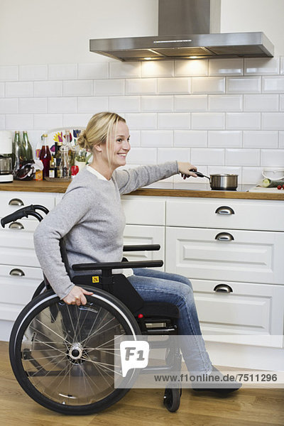 Glückliche behinderte Frau im Rollstuhl beim Zubereiten von Tee in der Küche