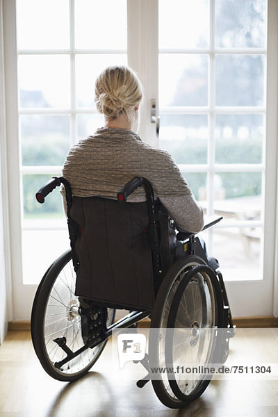 Rückansicht der behinderten Frau im Rollstuhl gegen Fenstertüren