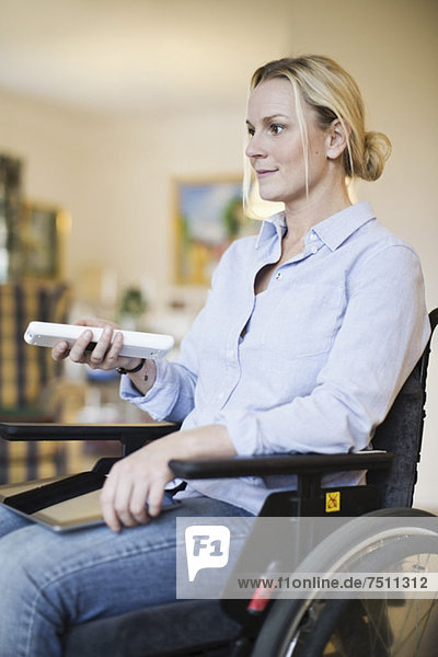 Behinderte Frau im Rollstuhl mit digitalem Tablett per Fernbedienung