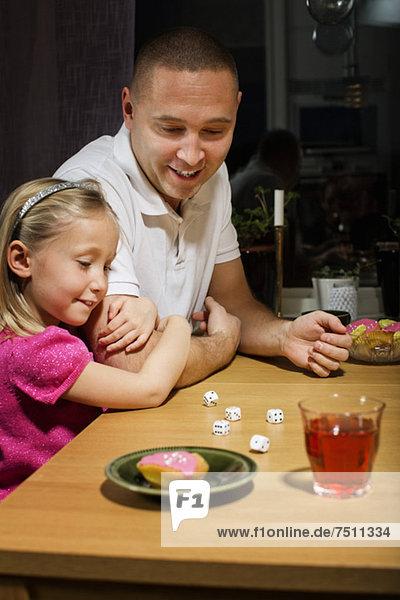Father and daughter playing with dice game at table