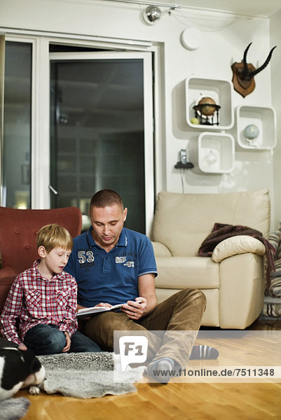 Father and son reading book while sitting on floor in living room