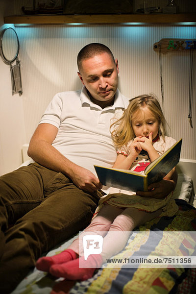 Vater und Tochter lesen gemeinsam im Bett.