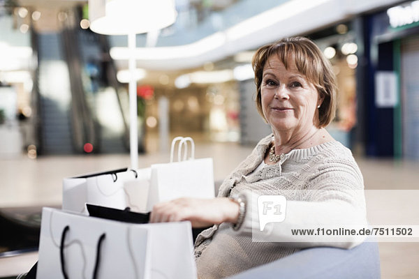 Happy senior woman with shopping bags sitting on sofa at mall