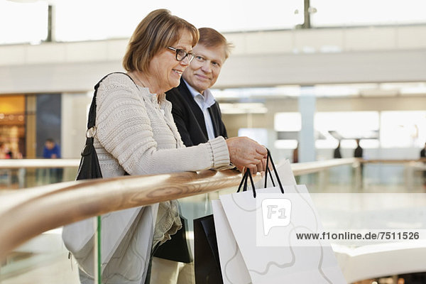 Happy senior woman with man standing by railing in shopping mall