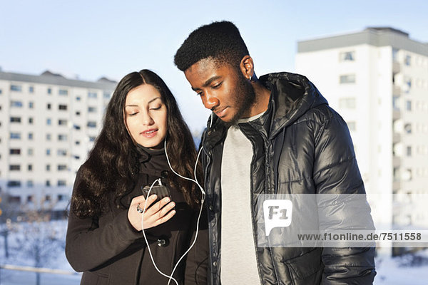 Young friends listening music through hands-free device against buildings